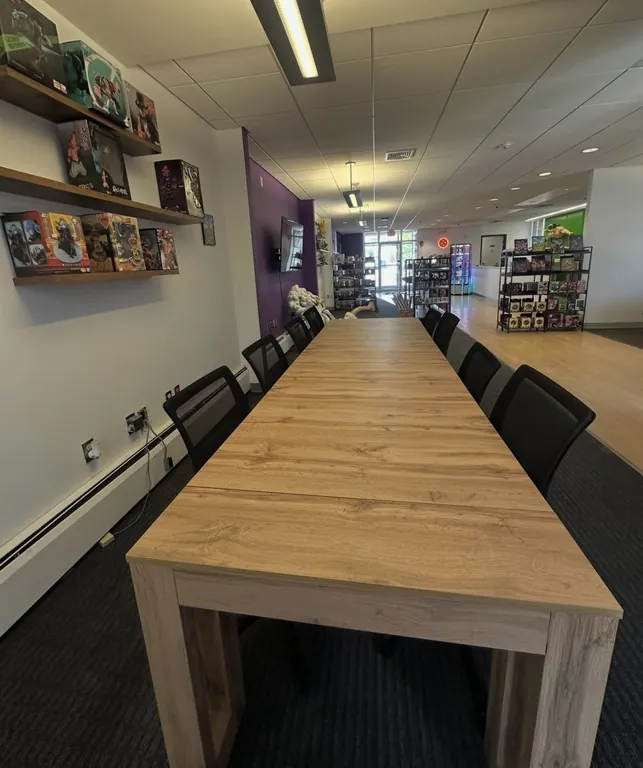 Long light-wood table with eight black chairs, card shelves along the left wall