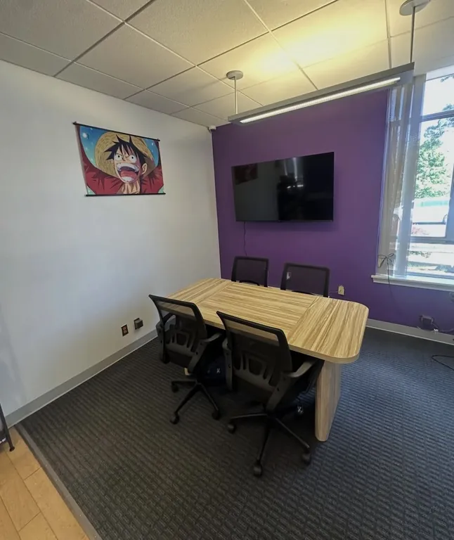 Back room with a Luffy wanted poster, a wall-mounted TV, purple wall, and a table with four chairs