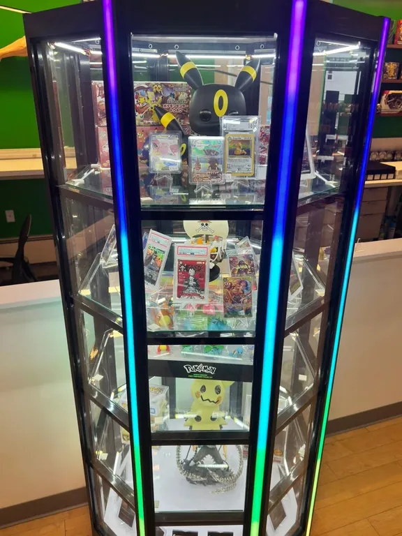 Tall lit glass tower of Funko Pops and figures beside a green wall