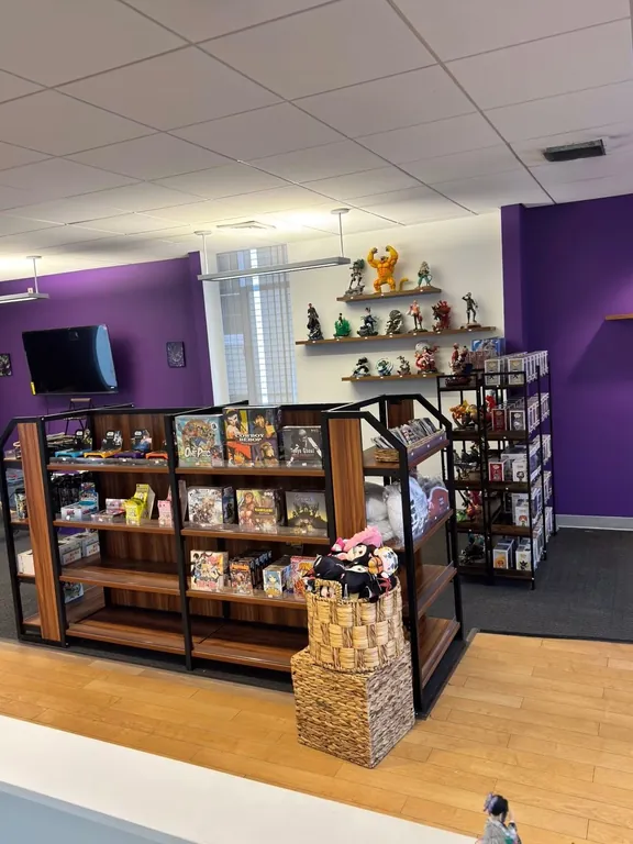 Black shelves of anime figures against brick, manga on the wall, and Catan boxes on the floor